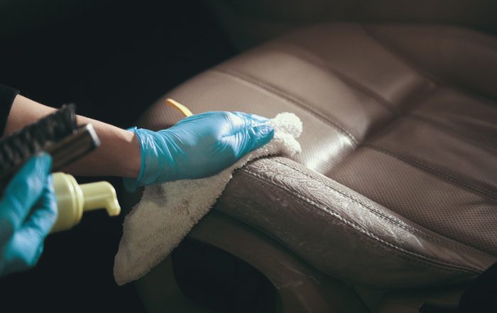 Worker in gloves is washing with brush a car seats, close up
